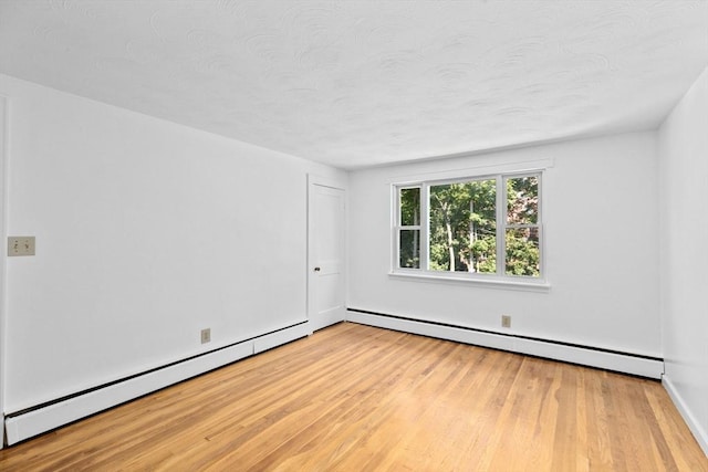 empty room featuring light wood finished floors, baseboard heating, and a textured ceiling