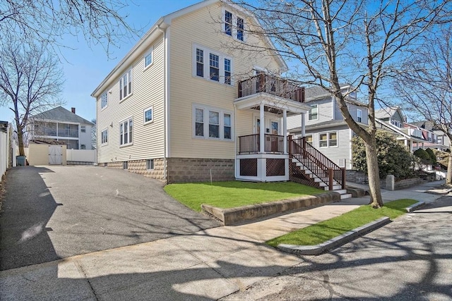 exterior space featuring fence, aphalt driveway, stairs, a lawn, and a balcony