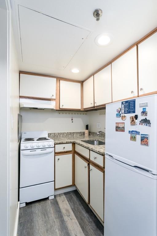 kitchen featuring white appliances, dark wood-type flooring, under cabinet range hood, white cabinetry, and a sink