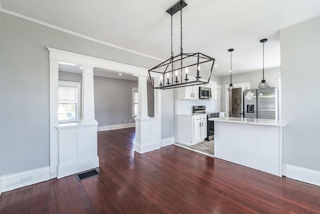 kitchen featuring appliances with stainless steel finishes, ornate columns, hardwood / wood-style flooring, light countertops, and decorative backsplash