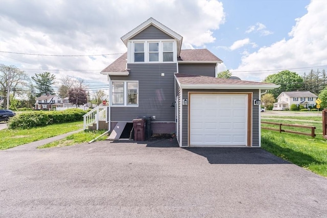 view of front facade featuring driveway, roof with shingles, fence, and an attached garage
