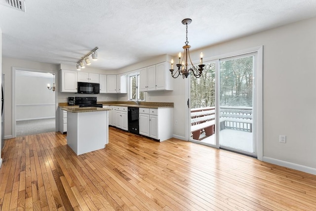 kitchen with an inviting chandelier, black appliances, a center island, pendant lighting, and white cabinets