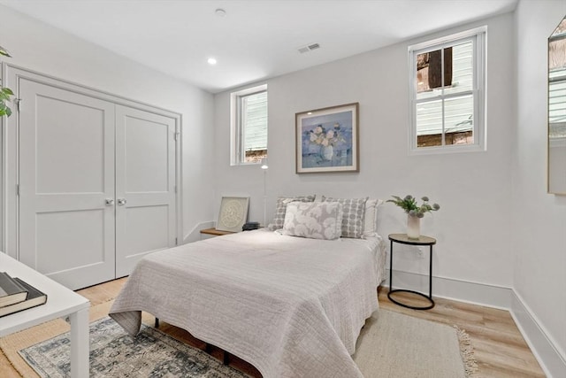 bedroom featuring multiple windows, light hardwood / wood-style flooring, and a closet