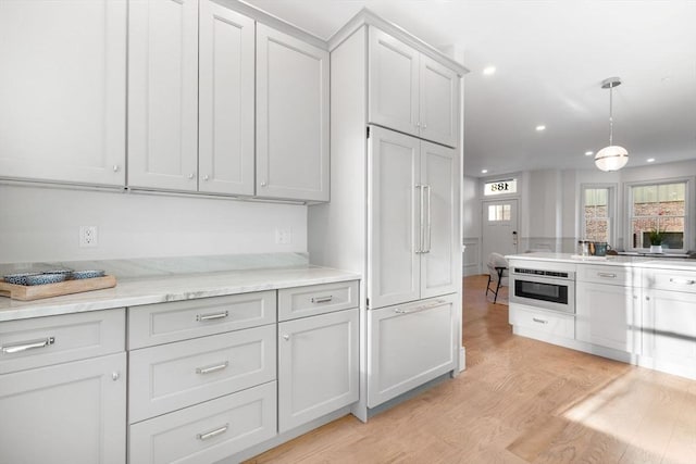 kitchen with light stone counters, wall oven, decorative light fixtures, and light wood-type flooring