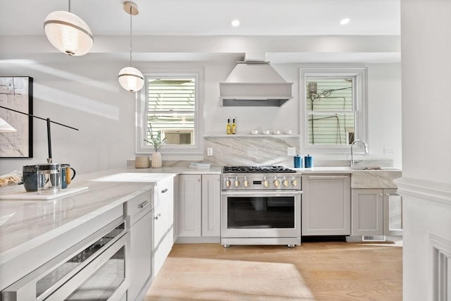 kitchen featuring premium range hood, sink, decorative light fixtures, light wood-type flooring, and high end stove