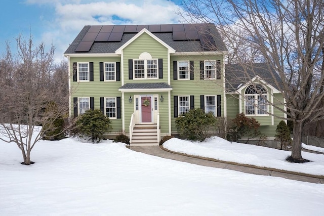 colonial inspired home with a shingled roof and roof mounted solar panels