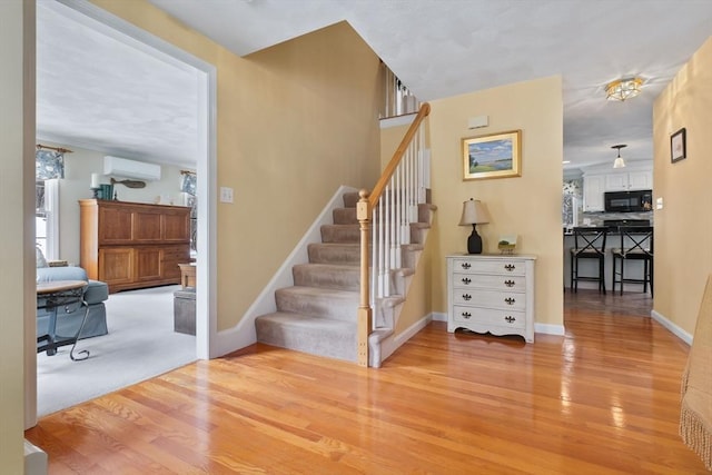 staircase with a wall unit AC, baseboards, and wood finished floors