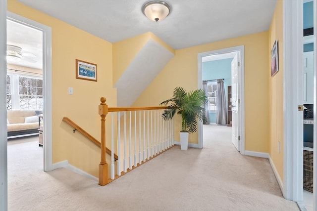 hallway featuring carpet, baseboards, and an upstairs landing