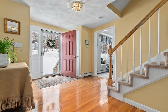 foyer with stairway, plenty of natural light, a baseboard heating unit, and wood finished floors