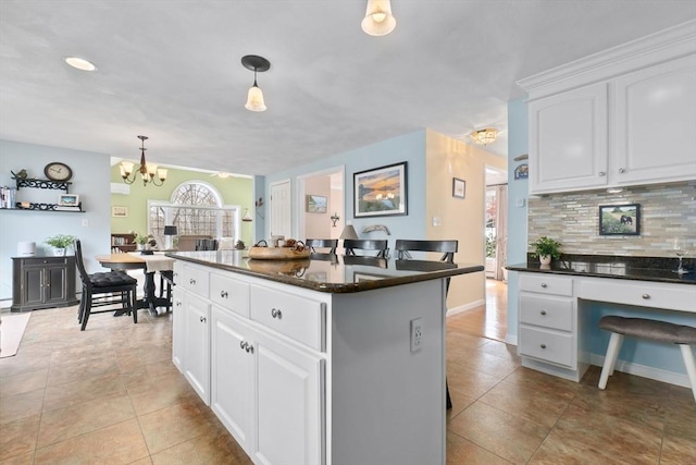 kitchen with dark countertops, white cabinetry, backsplash, and a center island