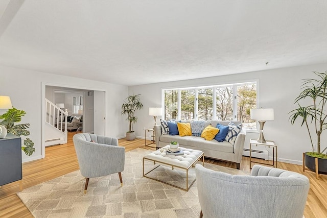 living room with a baseboard heating unit, stairway, baseboards, and light wood-style floors