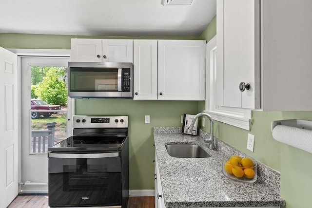 kitchen with stainless steel appliances, a sink, white cabinetry, and light stone countertops
