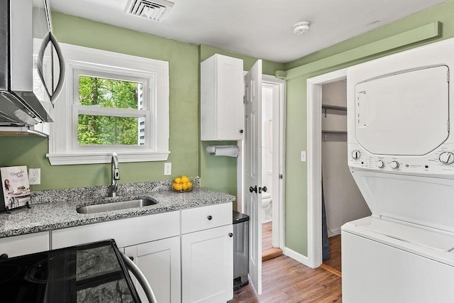 clothes washing area featuring stacked washer and clothes dryer, light wood-style floors, and baseboards