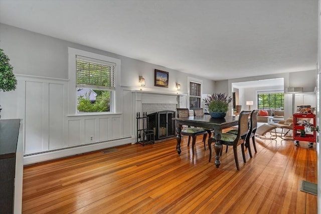 117 Parker Rd, Barnstable, MA 02655 - dining room featuring a baseboard radiator, a brick fireplace, a decorative wall, a wainscoted wall, and wood finished floors