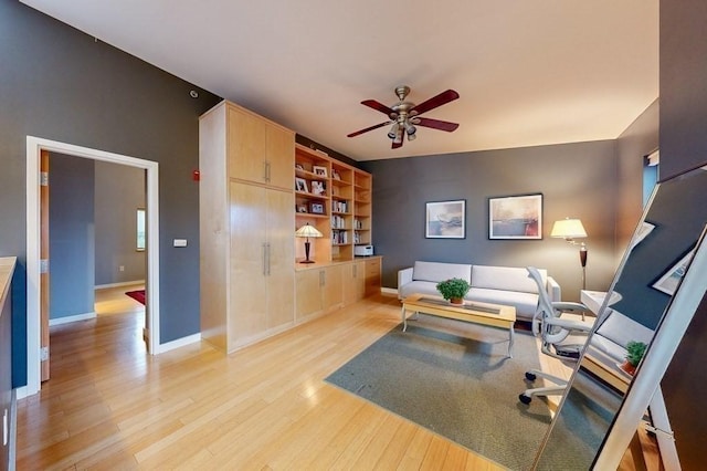 living area featuring ceiling fan, light wood-style flooring, and baseboards