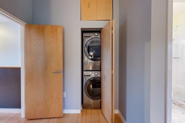 laundry room with stacked washer and dryer, light wood-type flooring, laundry area, and baseboards