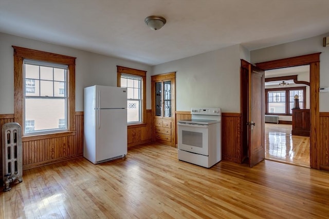 174 Vernon St, Worcester, MA 01610 - kitchen featuring white appliances, wainscoting, light wood-style floors, radiator heating unit, and plenty of natural light