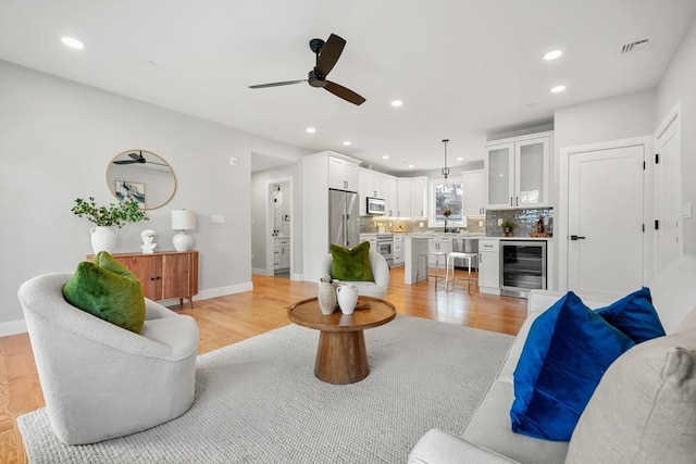 living room featuring light hardwood / wood-style flooring, wine cooler, ceiling fan, and sink