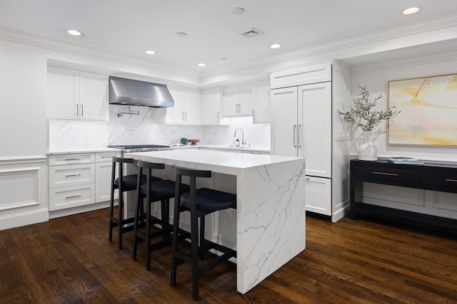 kitchen featuring crown molding, light stone counters, wall chimney range hood, and dark hardwood / wood-style flooring