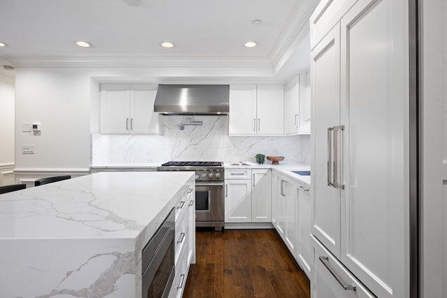 kitchen featuring dark hardwood / wood-style floors, light stone countertops, appliances with stainless steel finishes, ornamental molding, and wall chimney range hood