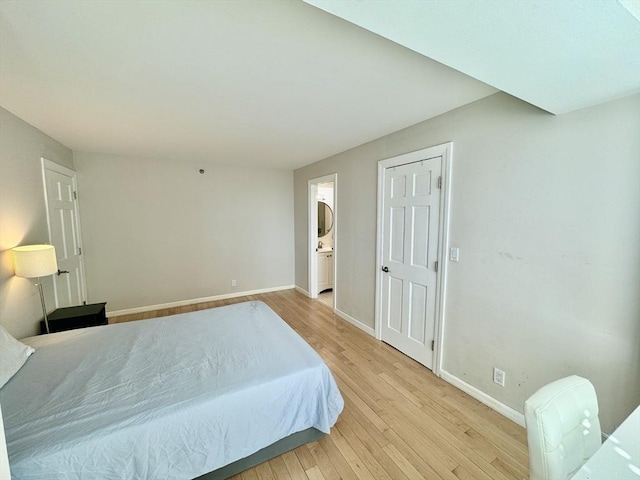 bedroom with ensuite bathroom, light wood-style flooring, and baseboards