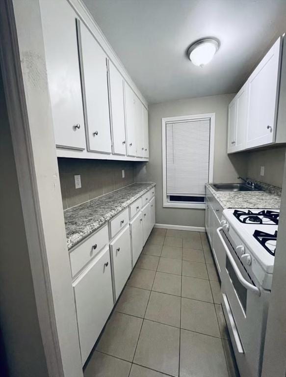 kitchen featuring light tile patterned floors, a sink, white cabinetry, baseboards, and white gas range oven