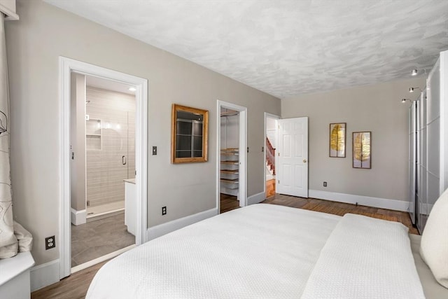 bedroom featuring a closet, wood finished floors, baseboards, a spacious closet, and ensuite bath