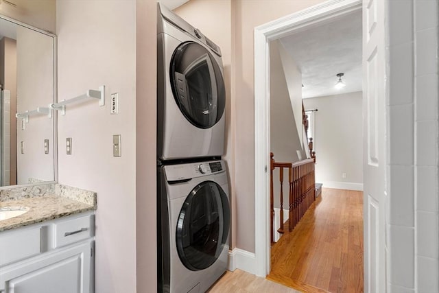washroom featuring laundry area, baseboards, light wood-style flooring, and stacked washer / drying machine
