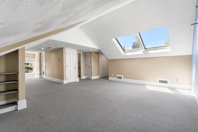 additional living space with visible vents, lofted ceiling with skylight, and carpet floors