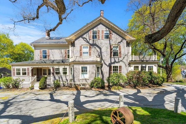 view of front of house with a porch, a chimney, and solar panels