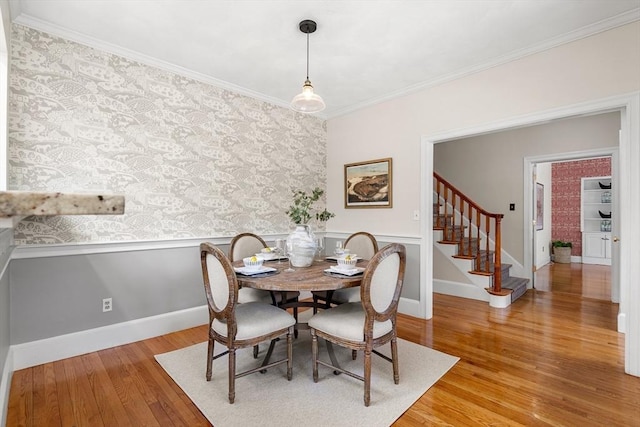 dining area featuring crown molding, stairs, wainscoting, wood finished floors, and wallpapered walls