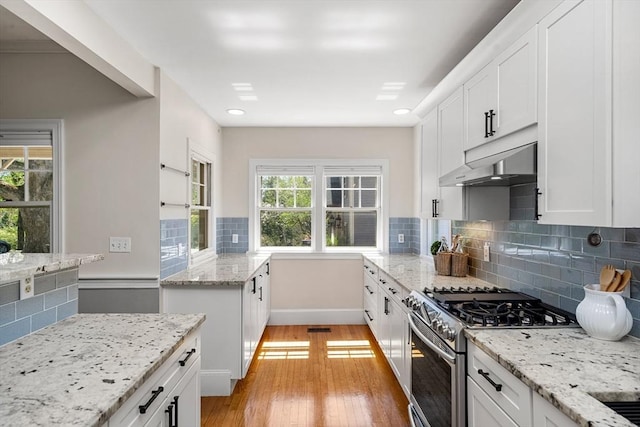 kitchen with stainless steel range with gas stovetop, white cabinetry, backsplash, light wood-type flooring, and under cabinet range hood