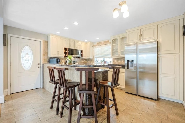 kitchen with stainless steel appliances, cream cabinets, tasteful backsplash, dark countertops, and recessed lighting