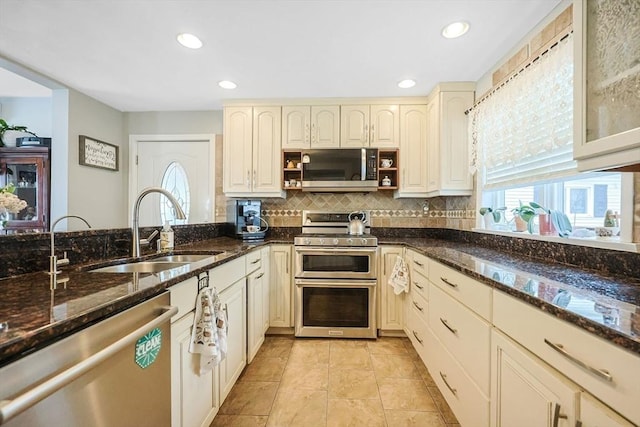 kitchen with stainless steel appliances, a sink, backsplash, recessed lighting, and dark stone counters