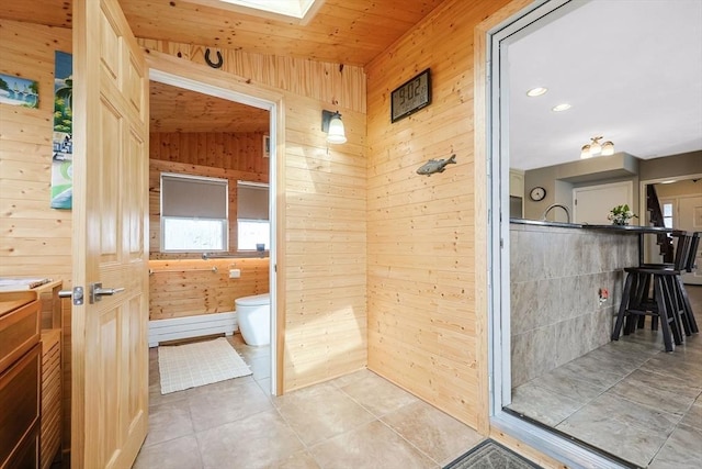 full bath featuring wooden walls, toilet, vanity, tiled shower, and tile patterned floors