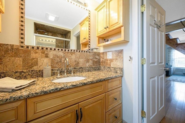 bathroom with decorative backsplash, wood finished floors, vanity, tiled shower, and ornamental molding