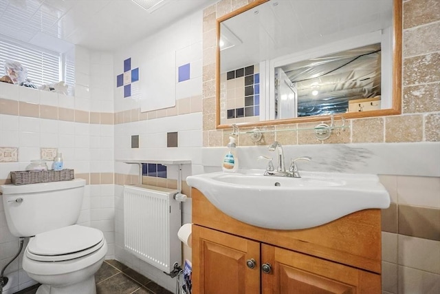 half bath with tile walls, radiator, tile patterned floors, toilet, and vanity