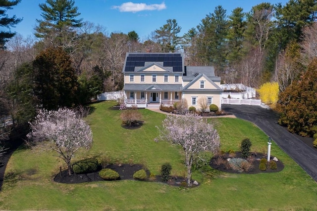 view of front of property with roof mounted solar panels, aphalt driveway, a porch, and a front lawn