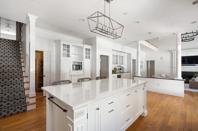 kitchen featuring light wood-type flooring, a center island, white cabinetry, and decorative columns