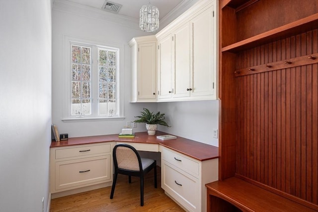 unfurnished office featuring built in desk, visible vents, ornamental molding, a chandelier, and light wood-style flooring