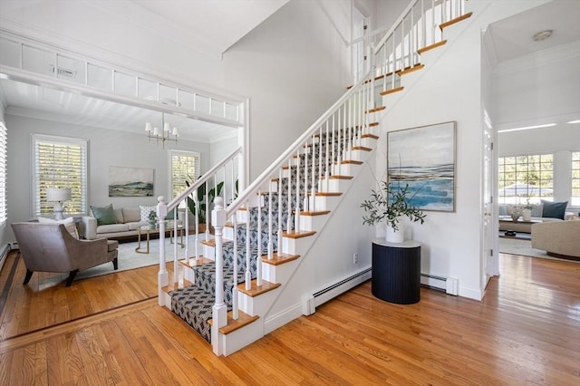 staircase featuring wood finished floors, crown molding, baseboards, a baseboard radiator, and a notable chandelier