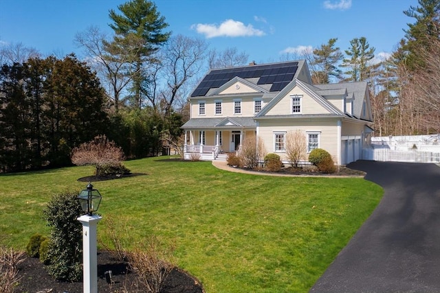 view of front of home featuring a chimney, a front lawn, aphalt driveway, a porch, and solar panels