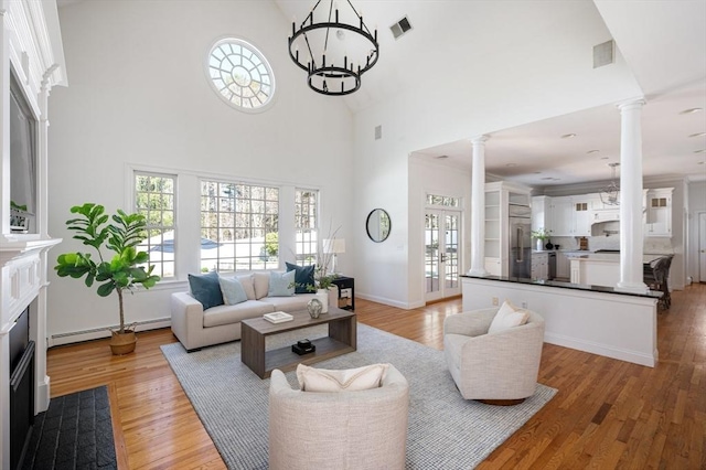 living area with plenty of natural light, decorative columns, visible vents, baseboard heating, and high vaulted ceiling