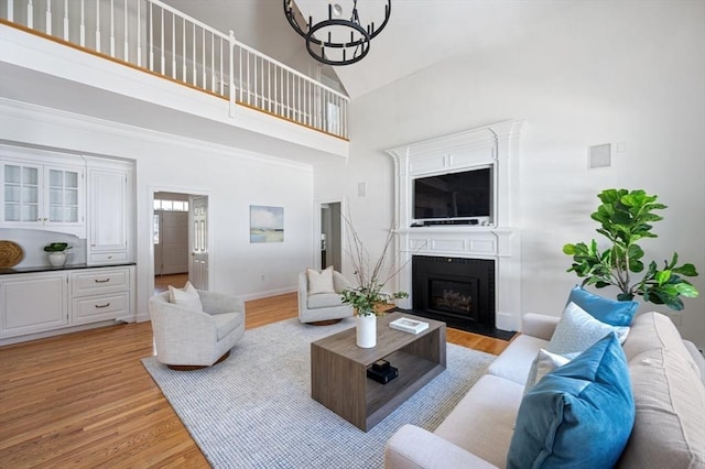living area featuring a fireplace with flush hearth, light wood-style floors, baseboards, a chandelier, and high vaulted ceiling
