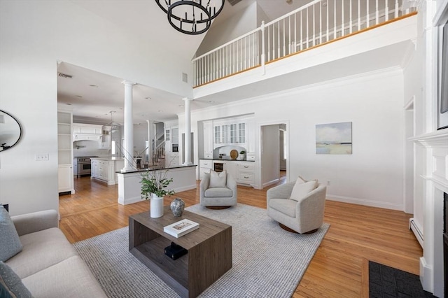 living room with light wood finished floors, a baseboard heating unit, decorative columns, a high ceiling, and a fireplace