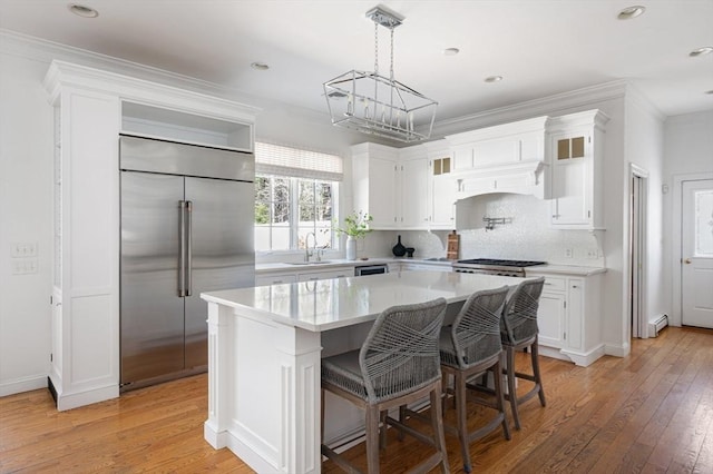 kitchen with light countertops, built in refrigerator, white cabinetry, and a sink