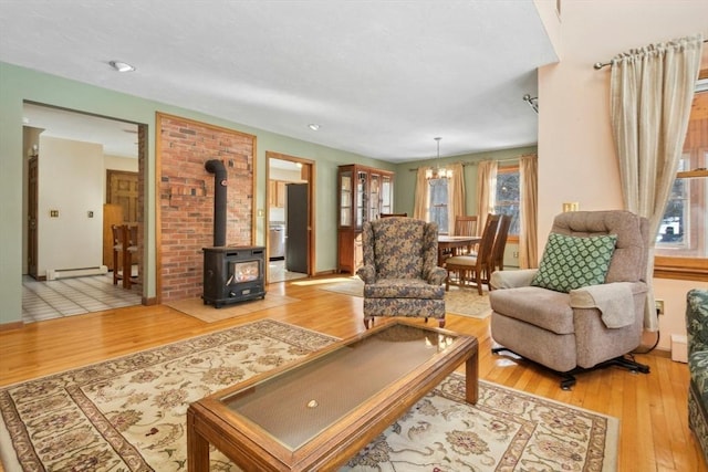 living room with a baseboard heating unit, a chandelier, a wood stove, and light wood-type flooring