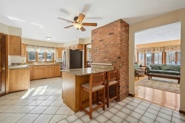 kitchen featuring light stone countertops, a healthy amount of sunlight, stainless steel refrigerator, and kitchen peninsula