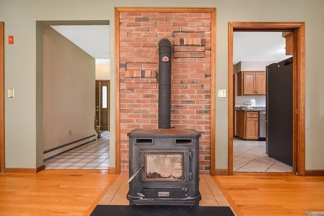 interior details with a baseboard radiator, wood-type flooring, stainless steel fridge, and a wood stove