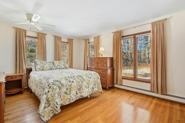 bedroom with ceiling fan, light wood-type flooring, and a baseboard heating unit